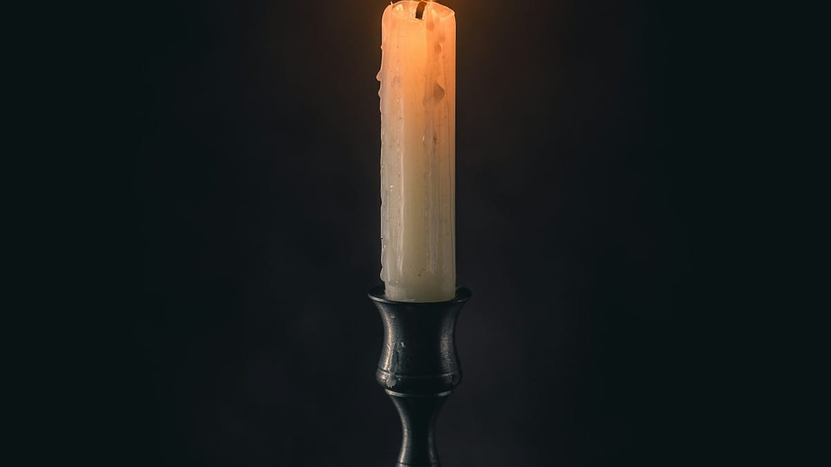 Una vela encendida ilumina suavemente un fondo oscuro.