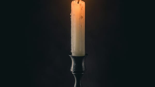 Una vela encendida ilumina suavemente un fondo oscuro.